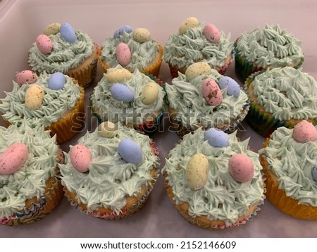 The top down, close up view of cupcakes that are decorated for Easter. There are a dozen cupcakes, all with green frosting that looks like grass, and candies in the shape of eggs.