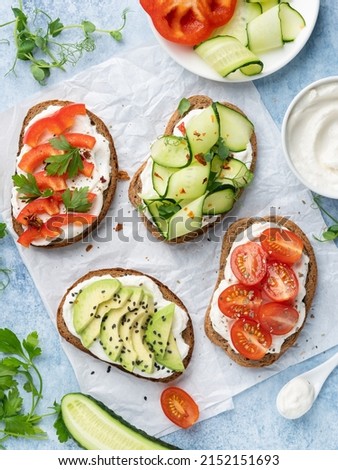 Open sandwiches variety, rye bread bruschetta with cream cheese (ricotta), cherry tomatoes, red pepper, cucumber slices dressed with dry herbs. Top view. Blue background. Healthy eating concept. Royalty-Free Stock Photo #2152151693