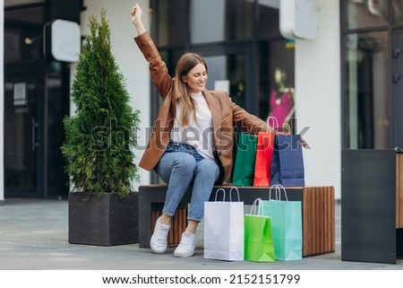 portrait of a smiling girl sitting near the mall. Girl holding colored shopping bags. The concept of shopping. Sale