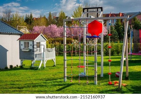 Green garden with a beautiful wooden house for children and a playground at blooming spring.