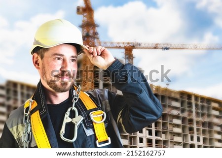 A male builder in a white hard hat against a blurred background of a construction site with a blue sky. Positive civil engineer with a beard
