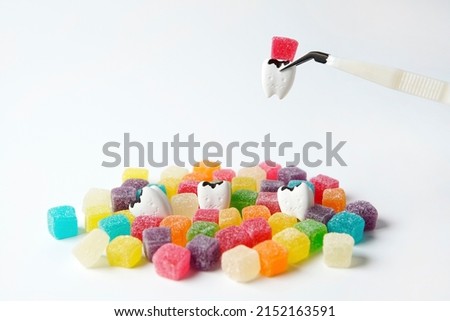 Cavity and tooth decay  pinching by clamp with a lot of colorful sweet sugar jelly candy on white background                                                                                   