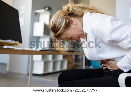 Middle aged businesswoman having stomach ache during work in office. Business woman experiencing abdominal cramps Royalty-Free Stock Photo #2152179797