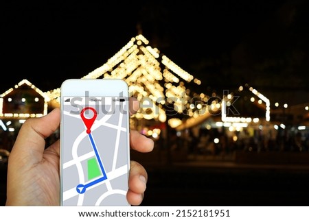 Man's hand holding white smartphone with GPS navigation application map with route plotted on screen. Night view of street blur on background.