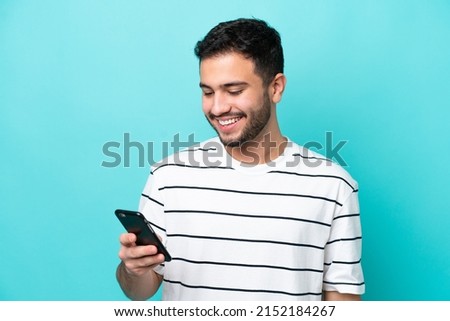 Young Brazilian man isolated on blue background sending a message or email with the mobile Royalty-Free Stock Photo #2152184267