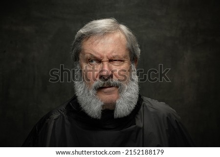 Dramatic actor. Half-length portrait of emotional senior bearded man getting beard grooming isolated on dark vintage background. Concept of emotions, fashion, beauty, self-reinvention