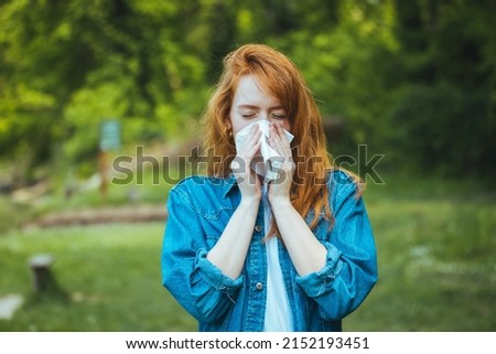 Young pretty woman blowing nose in front of blooming tree. Spring allergy concept. Attractive young adult woman coughing and sneezing outdoors. Sick people allergy or virus influenca concept. Royalty-Free Stock Photo #2152193451