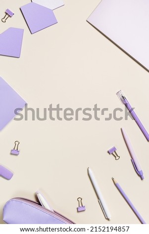 Frame with notebook violet color, pencils, pens, paper clips, pencil case, school stationery flat lay. Back to school concept on beige background, copy space. Office supplies on table, top view