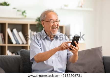 Happiness of wellness elderly asian man with white hairs sitting on sofa using mobile phone and social media smile at home.Cheerful Senior using cellphone relax and resting with online lifestyle Royalty-Free Stock Photo #2152206731