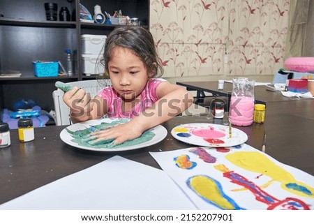 Cute adorable baby girl learning drawing and painting with poster colors at home. 

