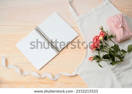 Blank diary with a pink rose, gift wrapped in cloth, apron on a wooden background. Space for text. Flat lay. Florist concept. High quality photo