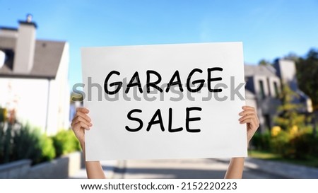 Woman holding sign with text GARAGE SALE on street, closeup