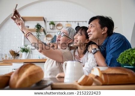 Happy Asian family cooking together and preparing delicious organic food in kitchen. Take a photo and smiling while making organic salad for breakfast.