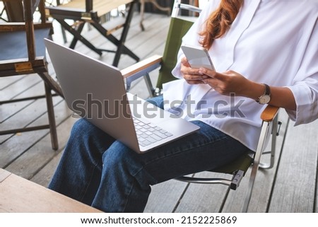Closeup image of a woman holding and using mobile phone and laptop computer 