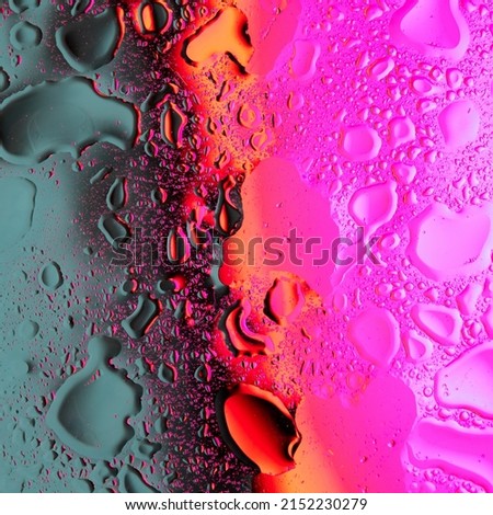 A macro shot of mixed drops of oil and water on a glass surface illuminated by bright neon light in color gradation. Abstract vivid bold colors background.