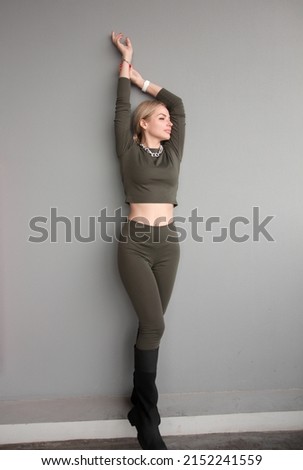 teen walk style. young fit blonde girl in slim khaki suit stands casual with cute smile in pose on the gray wall background at street and looks apart with hands up. lifestyle concept, free space
