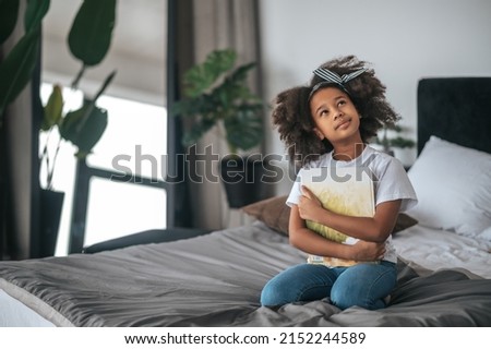 A curly-haired girl sitting on bed and looking dreamy Royalty-Free Stock Photo #2152244589