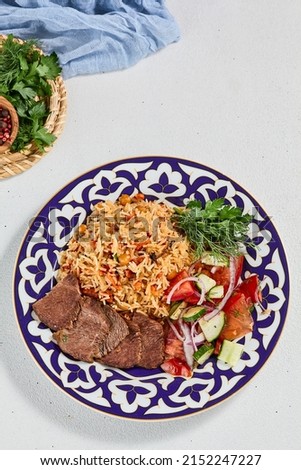 Traditional uzbek food - plov with beef. Eastern cuisine - pilaf with rice, meat and spices. Plov with beef on traditional uzbek plate. Composition of oriental ceramic plate with pilaf Royalty-Free Stock Photo #2152247227