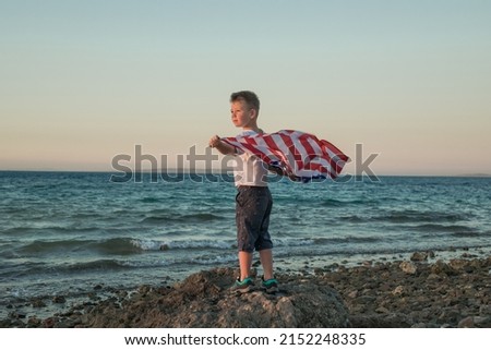 Little boy lets the american flag fly in his hands on the wind at the Sea. Patriotic family celebrates usa independence day on 4th of July.