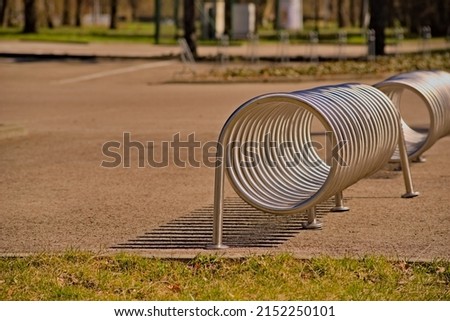 Bicycle parking rack, made of a steel, stainless steel tube twisted in a spiral. The stand is set on a paved surface near the park.