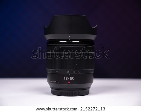 Zoom lens with a focal length of 12-60mm stands on a white table on a black background