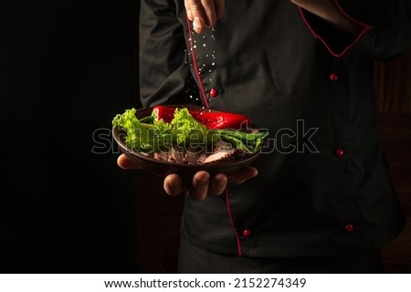 The chef sprinkles salt on a sliced steak with beef and vegetables in a plate. The concept of serving dishes to order. Asian cuisine