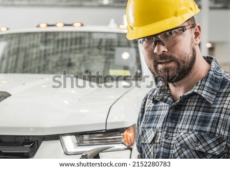 Portrait of a Caucasian General Construction Contractor Worker in His 30s Wearing Yellow Hard Hat. Pickup Truck in the Background