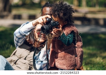 Beautiful multiracial family relaxing in the park during a sunny day and using a digital camera. Photographing memories. African american baby girl holding a camera. Baby girl holding a camera.