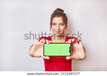 Pretty girl holding a smartphone with a green display. Demonstration of the image on the smartphone screen.