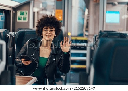 Portrait of a young woman with afro hair using smartphone and waving with her hand while traveling by train. Enjoying travel concept.