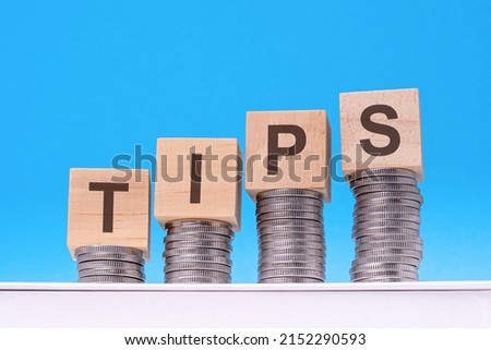 tips - text on wood cube block stack with coins, blue background, business concept