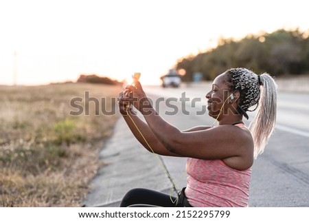 African American woman sitting on the side of the road taking a selfie after exercising. 