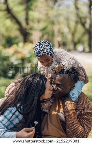 Caucasian and african american diverse family relaxing while spending time together in the park on a weekend. Unconditional love between parents and children. Beautiful childhood. Parents kissing.
