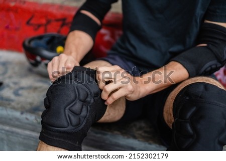 unrecognizable man putting on knee pads to ride rollers at a skate park