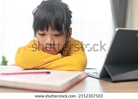 Little Asian girl sitting alone and looking out with a bored face, Preschool child laying head down on the table with sad  bored with homework, spoiled child