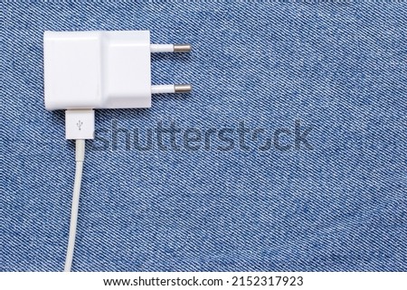 White plug for an outlet on a denim background. Charging plug on a blue denim with free space for text. Charger and electricity concept for gadgets and electronics for every day