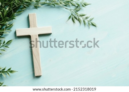 Wood cross with border of green leaves on a blue wood background with copy space