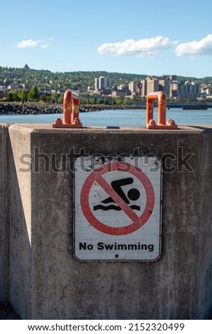 A vertical shot of a No swimming sign in front of a lake in a city