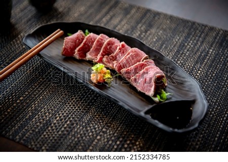 Beef tataki appetizer in the traditional Japanese ramen restaurant, with a black plate on a black mat in a black scene background Royalty-Free Stock Photo #2152334785