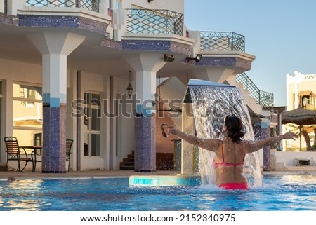 Woman enjoying under jet of hydromassage water with gentle splashes at spa resort. Waterfall flow in spa swimming pool. Hydrotherapy, health and skin care. Vacation concept. High quality photo