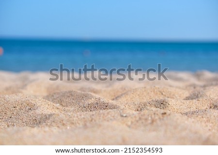 Close up of clean yellow sand surface covering seaside beach with blue sea water on background. Travel and vacations concept.