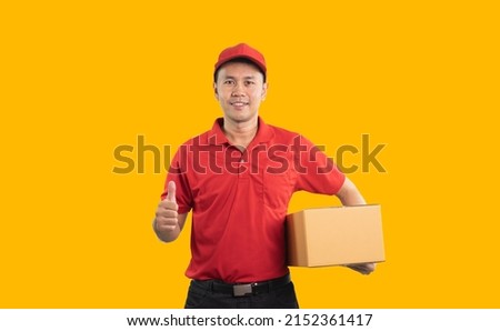 Asian delivery man worker smiling and thumbs up in red uniform isolated on yellow background, hold parcel boxes for sending or conveying parcels by mail. Royalty-Free Stock Photo #2152361417