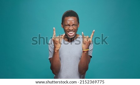 Funky cool man showing rock metal sign with hands in front of camera, expressing fun punk music with positive energy. Male hipster rocker gesturing devil horns symbol for entertainment.