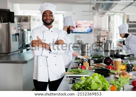 Gastronomy expert standing in restaurant professional kitchen with arms crossed while smiling at camera. Confident head chef wearing cooking uniform while preparing ingredients for dinner service. Royalty-Free Stock Photo #2152369853