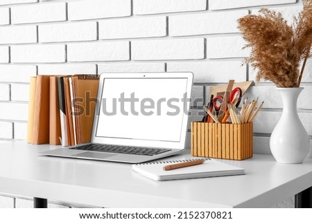 Workplace with laptop, stationery and pampas grass in vase near white brick wall