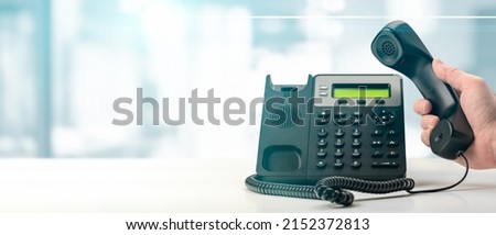 Dialing landline telephone keypad concept for communication, contact us and customer service support. hand holding voip telephone receiver on blurred office background. banner Royalty-Free Stock Photo #2152372813
