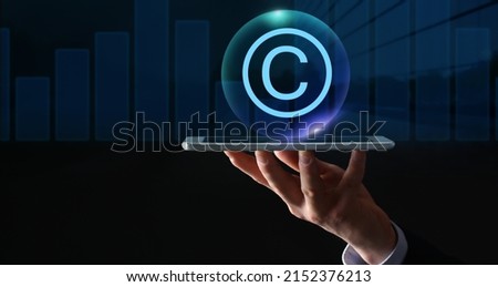 Hand of businessman holding tablet computer and symbol of copyright on dark background