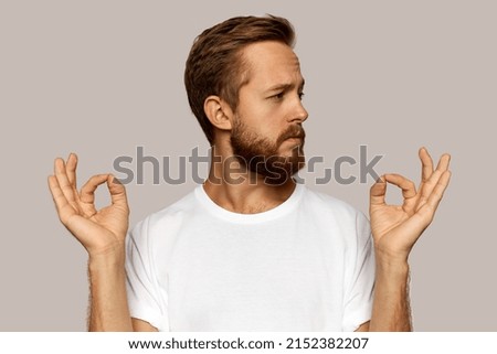 Profile view of redhead brutal guy of 30s keeping hands in mudra, frowning, looking serious with skeptical facial expression against gray background. Body language, signs, gestures concept