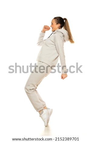 a young woman in a gray tracksuit poses against a white background in the studio