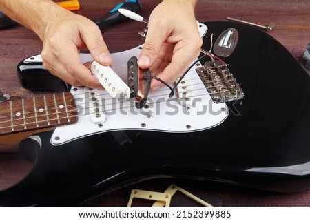 Guitar repairman selects a pickup for replacement on electric guitar. Royalty-Free Stock Photo #2152399885